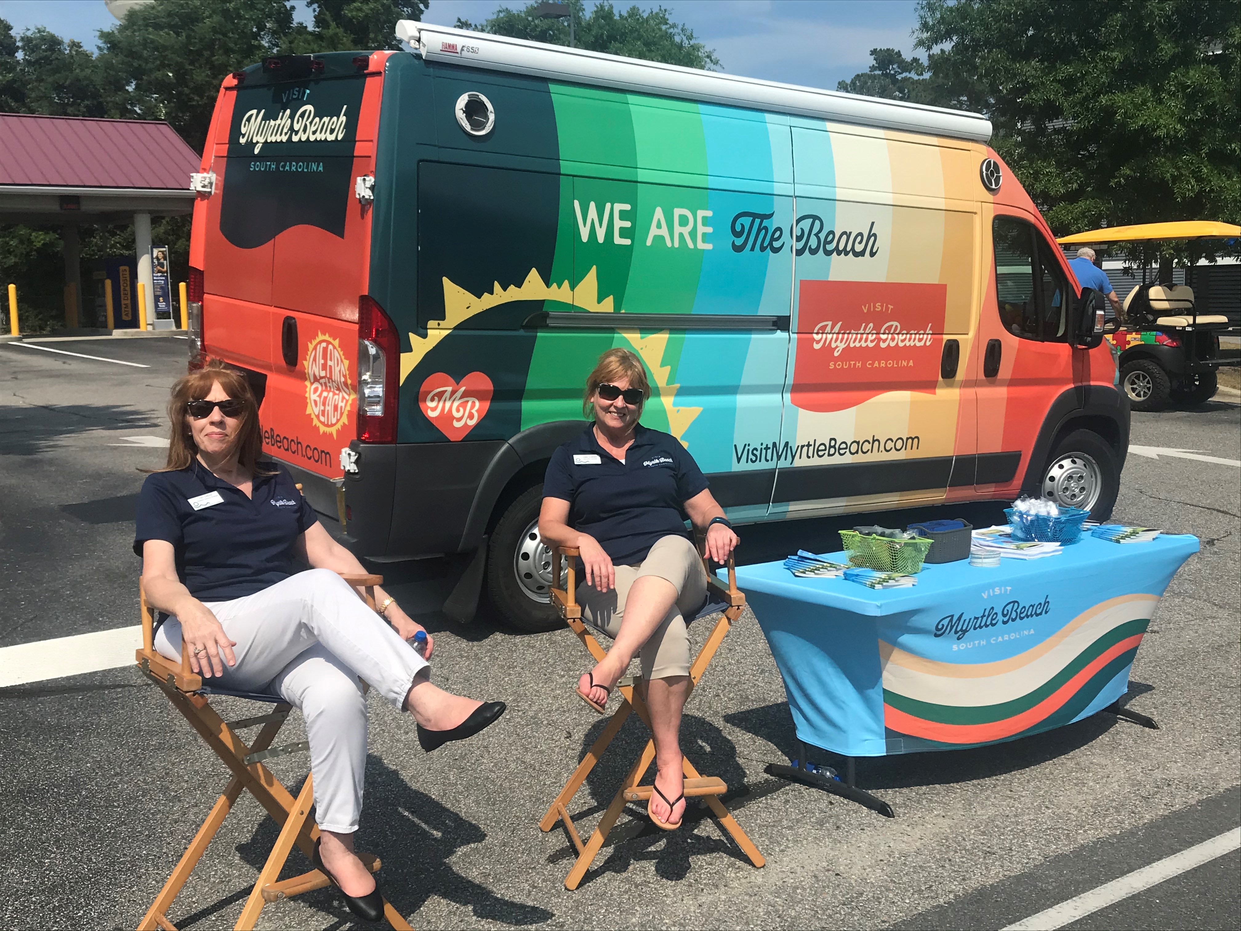 two women sit in front of van that says we are the beach visit myrtle beach